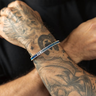 Tattooed arm wearing a blue and silver bracelet against a dark background