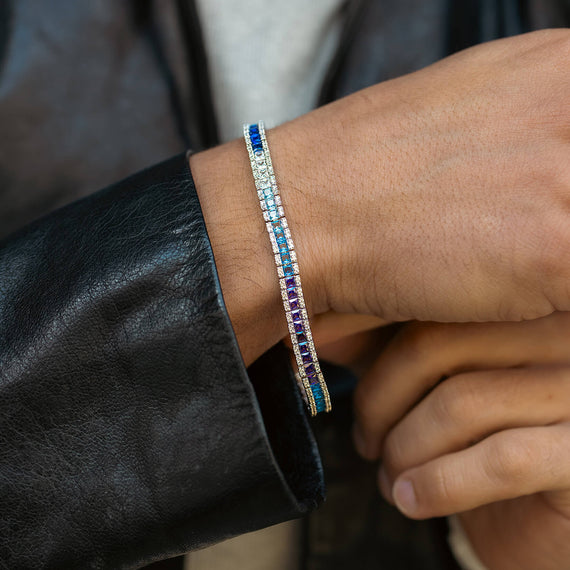 Close-up of a hand wearing a blue iced bracelet on a dark sleeve.