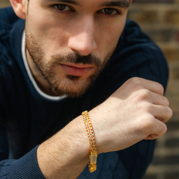 Man wearing a gold bracelet with a blurred brick wall background