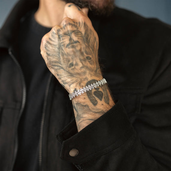Person wearing a black jacket with a tattooed arm and Iced silver bracelet.