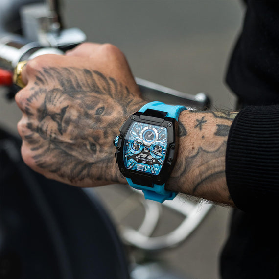 The Intrepid Sport - Arctic Blue men's luxury watch featuring a bold blue strap, black rectangular case, and intricate dial with chronograph subdials, worn on a tattooed wrist, statement luxury watch by Ralph Christian. Bold by Design.
