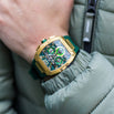The Intrepid Sport - Gold men's luxury watch featuring a bold gold case with green accents, chronograph subdials, and a green strap, worn on wrist with a casual jacket.