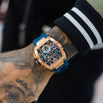 The Intrepid Sport - Rose Gold men's luxury watch featuring a bold rose gold case, intricate chronograph subdials, and a vibrant blue strap, worn on a tattooed wrist.