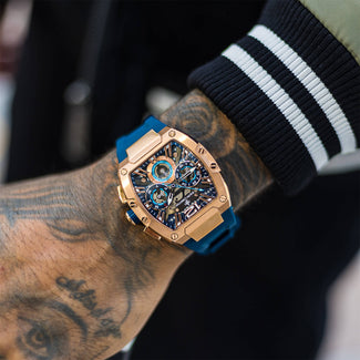 The Intrepid Sport - Rose Gold men's luxury watch featuring a bold rose gold case, intricate chronograph subdials, and a vibrant blue strap, worn on a tattooed wrist.