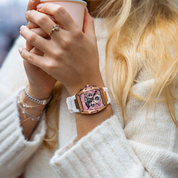 The Intrepid Sport Ladies - Sakura Blush rose gold watch with a pink detailed dial and white strap shown on a woman's wrist in a cozy lifestyle setting