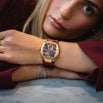 The Intrepid Sport Ladies - Scarlet Gold luxury watch on a woman's wrist with a gold tone case, detailed dial, burgundy leather strap, and layered bracelets