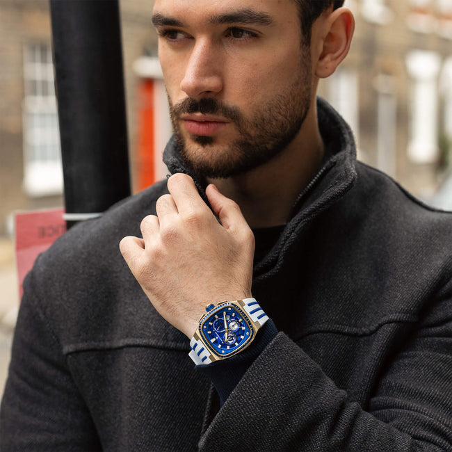 Man wearing The Legacy Chrono Ice - Sapphire Royale luxury watch with a bold blue dial, chronograph subdials, sapphire-coated crystal, and ice-set bezel paired with a white and blue striped strap, styled with a dark jacket in an urban setting. Bold by Design.