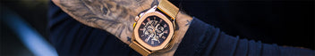 Close-up of a wrist wearing a bold rose gold luxury watch with chronograph subdials, black dial, and a matching rose gold metal bracelet, showcasing detailed craftsmanship.