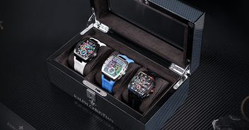 Three men's luxury watches with bold, detailed dials and varied straps in white, blue, and black, displayed inside a sleek black watch case with a glass lid.