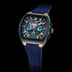 A luxury watch, featuring a square rose gold case, a black dial with blue sub-dials, and a dark blue silicone strap, set against a solid black background.