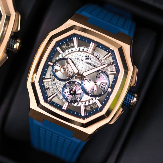 Luxury watch with blue strap and rose gold casing on a dark background