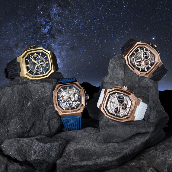 Four ornate watches on rocks with a starry night sky background