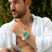 Man wearing The Legacy Chrono - Arctic Azure luxury men's watch with a bold Arctic blue dial and white strap, styled with layered gold necklaces and a white shirt, Bold by Design.