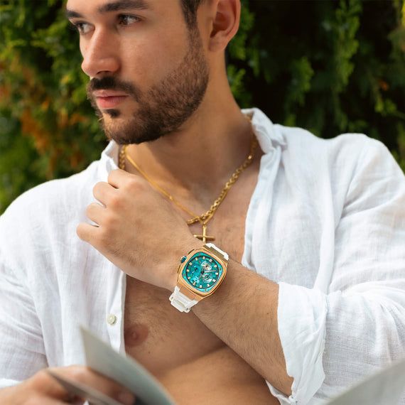 Man wearing The Legacy Chrono - Arctic Azure luxury men's watch with a bold Arctic blue dial and white strap, styled with layered gold necklaces and a white shirt, Bold by Design.