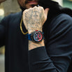 Person wearing a colorful watch on a tattooed wrist with a blurred background