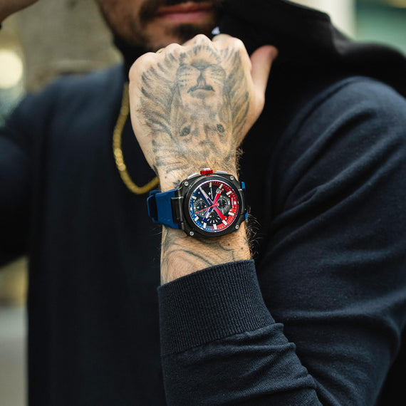 Person wearing a colorful watch on a tattooed wrist with a blurred background