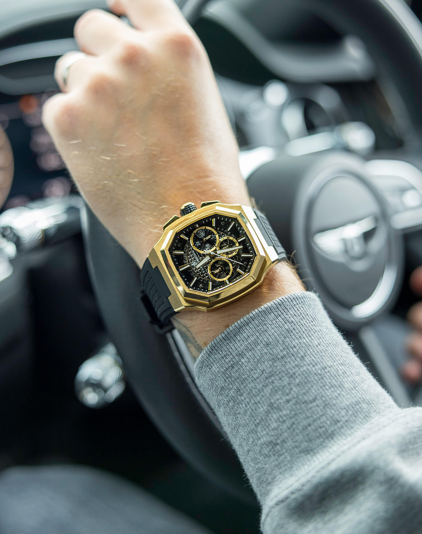 Person wearing a gold and black watch inside a car