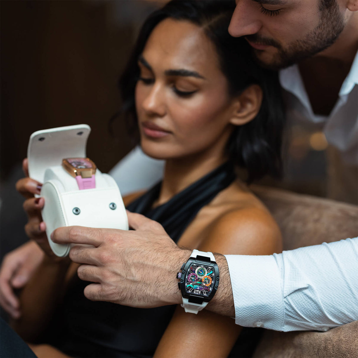 Couple viewing watches, with a silver-toned statement watch featuring a colorful dial and steel bracelet worn on a man's wrist.