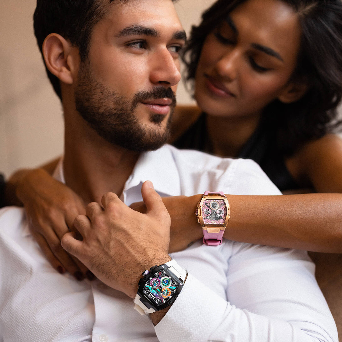 Couple embracing while wearing two colorful statement watches, including a pink watch on the woman and a black watch with a multicolor dial on the man