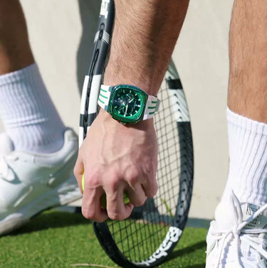 Person holding a tennis racket on a grass court with a watch on their wrist.