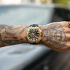 Gold and black wristwatch on a tattooed arm with a blurred background