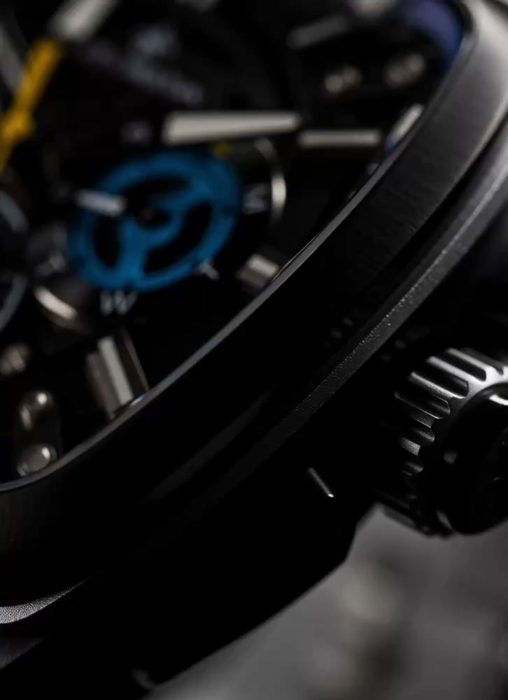 Close-up view of a black men's luxury watch dial featuring chronograph subdials with purple, blue, and white accents, yellow seconds hand, and luminous markers under sapphire-coated crystal.
