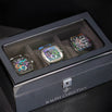 Luxury Collectors Watch Case with carbon fiber textured exterior and clear display lid, showcasing three automatic chronograph watches with colorful dials inside.